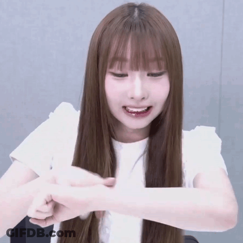 A Girl With Long Brown Hair And Bangs Is Smiling And Holding Her Hand To Her Face GIF