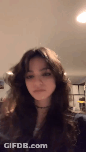 A Girl With Long Dark Hair Is Standing In A Room . GIF