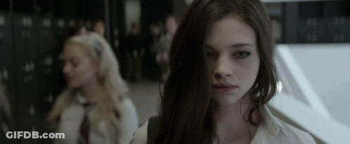 A Girl With Long Dark Hair Looks At The Camera In A Dark Room GIF