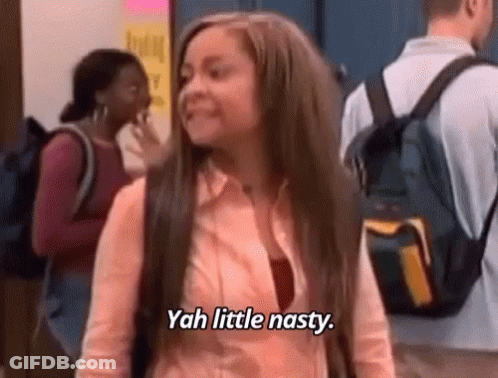 A Girl With Long Hair And A Backpack Is Standing In A Hallway And Says `` Yah Little Nasty '' . GIF