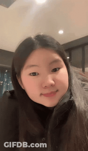 A Girl With Long Hair And A Black Shirt Is Smiling For The Camera GIF