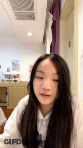 A Girl With Long Hair Is Sitting In A Room With A Ceiling Fan GIF