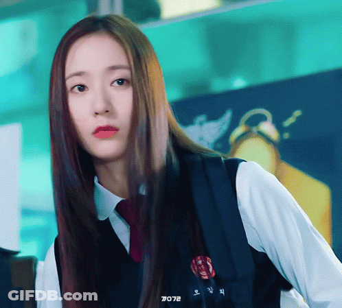 A Girl With Long Hair Is Wearing A White Shirt And A Black Vest With A Red Badge On It GIF