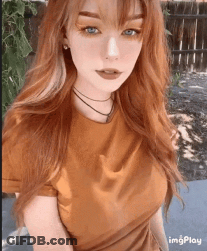 A Girl With Long Red Hair And Blue Eyes Is Wearing A Brown Shirt GIF