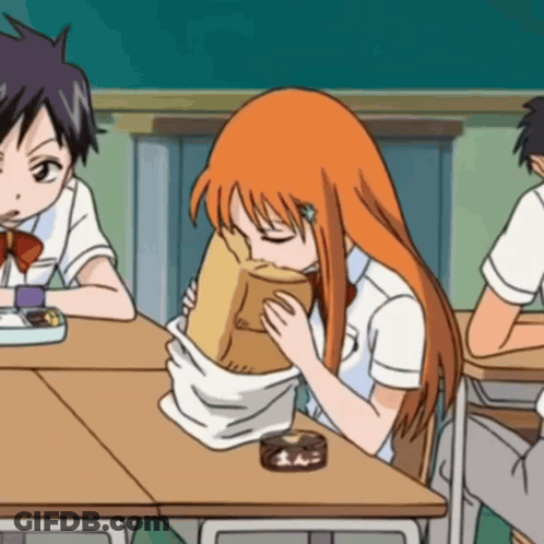 A Girl With Orange Hair Is Sitting At A Desk Eating From A Brown Paper Bag GIF