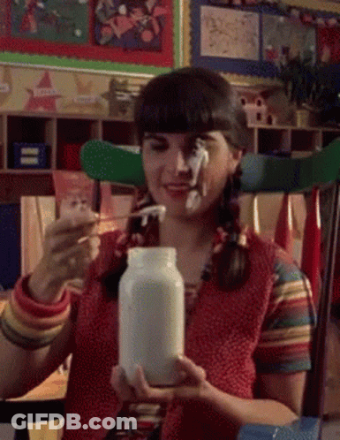 A Girl With Pigtails Is Holding A Jar Of Milk And A Spoon GIF