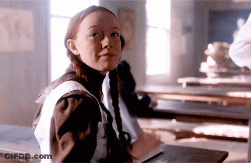 A Girl With Pigtails Is Sitting At A Desk With A Book GIF