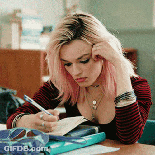 A Girl With Pink Hair Is Sitting At A Desk Writing In A Notebook . GIF