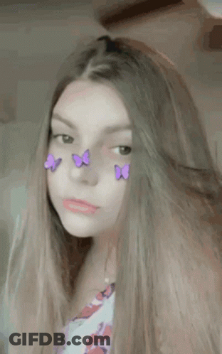 A Girl With Purple Butterflies On Her Face Is Looking At The Camera . GIF