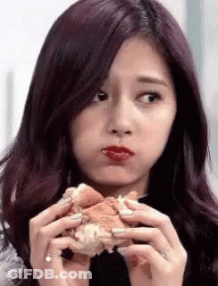 A Girl With Purple Hair Is Eating A Hamburger With Her Mouth Open . GIF