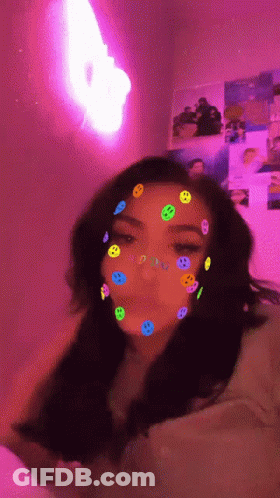 A Girl With Smiley Faces On Her Face And A Pink Light In The Background GIF