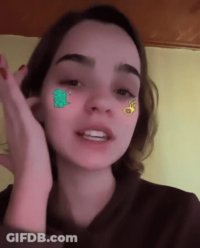 A Girl With Stickers On Her Face Including A Green Dinosaur GIF