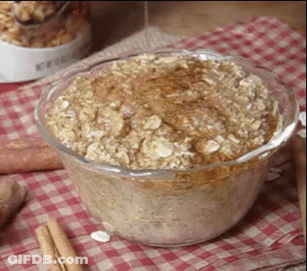 A Glass Bowl Filled With Oatmeal And Cinnamon Sticks On A Checkered Table Cloth . GIF
