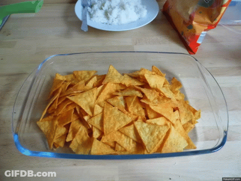 A Glass Dish Filled With Tortilla Chips Next To A Bag Of Tortilla Chips GIF