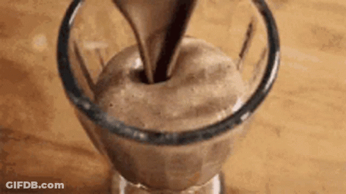 A Glass Of Chocolate Mousse Is Being Poured Into A Glass On A Table . GIF