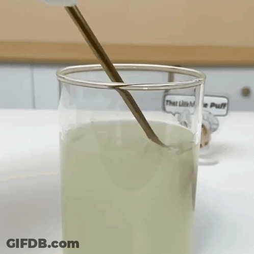 A Glass Of Liquid With A Spoon In It And A Sticker That Says That Little Puff GIF
