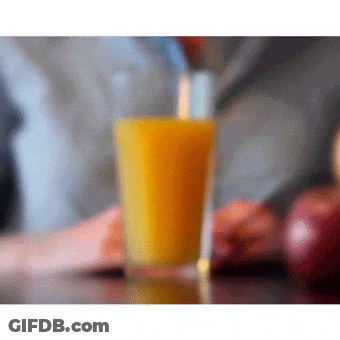 A Glass Of Orange Juice Is On A Table Next To Apples GIF