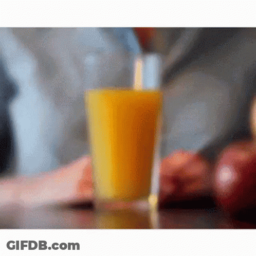 A Glass Of Orange Juice Is Sitting On A Table GIF