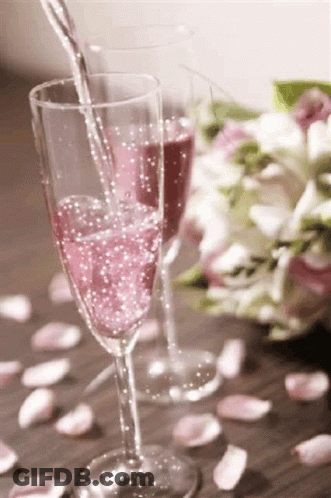 A Glass Of Pink Champagne Is Being Poured Into A Glass On A Table . GIF