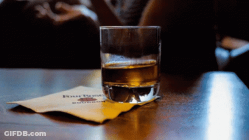 A Glass Of Whiskey Sits On A Napkin With Four Roses Written On It GIF