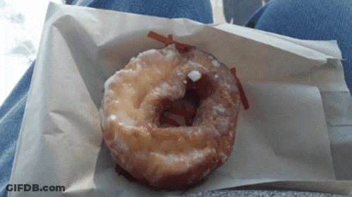 A Glazed Donut Is Sitting On A Piece Of Paper GIF