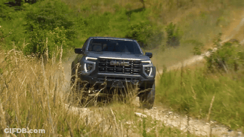 A Gmc Truck Is Driving Down A Dirt Path GIF