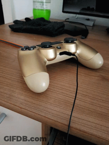 A Gold Video Game Controller Is Sitting On A Wooden Desk GIF