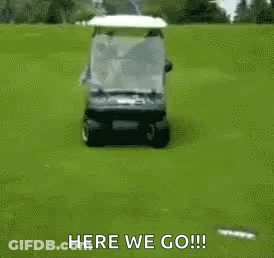 A Golf Cart Is Driving Down A Golf Course With A Person Sitting On The Back . GIF