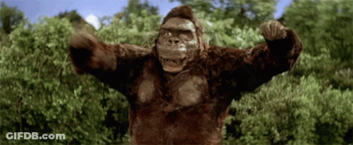 A Gorilla With Its Arms Outstretched Is Standing In Front Of Trees GIF