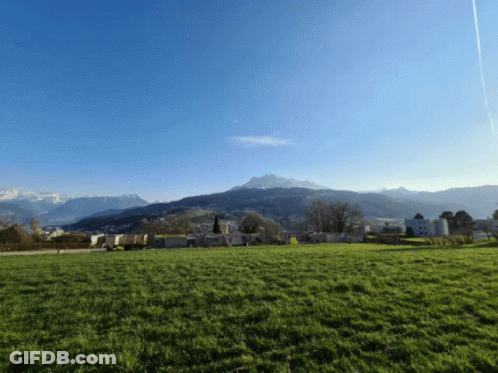 A Grassy Field With Mountains In The Background And A Blue Sky GIF