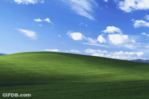 A Grassy Hill With A Blue Sky And White Clouds Behind It GIF