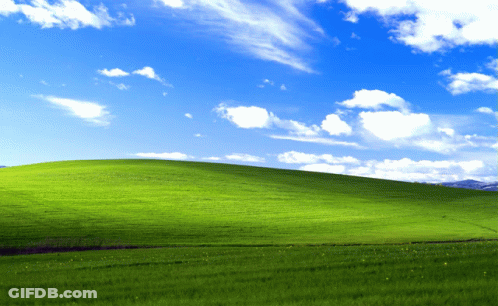 A Grassy Hill With A Blue Sky And White Clouds Behind It GIF