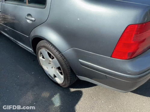 A Gray Car With A Red Tail Light Is Parked On The Side Of The Road GIF