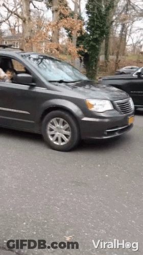 A Gray Chrysler Minivan Is Driving Down The Street GIF