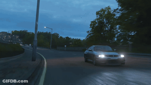 A Gray Sports Car Is Driving Down A Road With Trees In The Background GIF