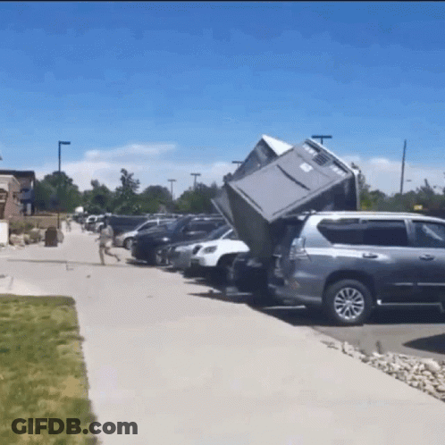 A Gray Suv Is Parked In A Parking Lot With A Fridge In The Back GIF