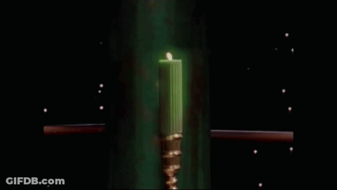 A Green Candle In A Gold Candle Holder Is Glowing In The Dark GIF