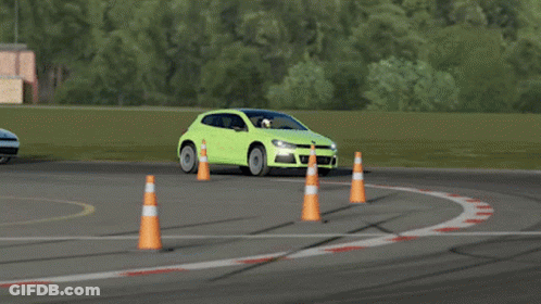 A Green Car Is Driving On A Race Track Next To A Traffic Cone GIF