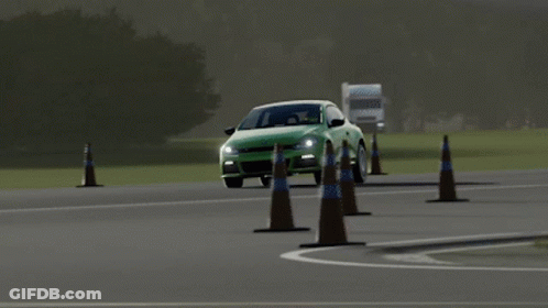 A Green Car Is Driving Past A Traffic Cone On A Road GIF