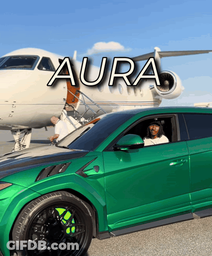 A Green Car Is Parked In Front Of A Plane That Says Aura On It GIF