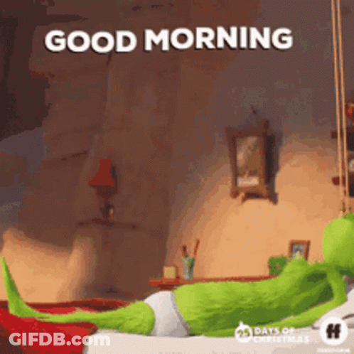 A Green Cartoon Character Is Laying On A Bed With The Words `` Good Morning '' Written Above Him . GIF