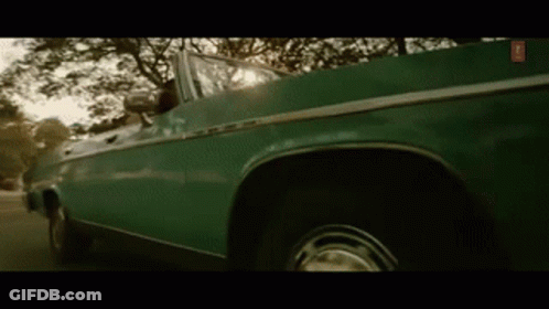 A Green Convertible Car Is Driving Down A Street . GIF