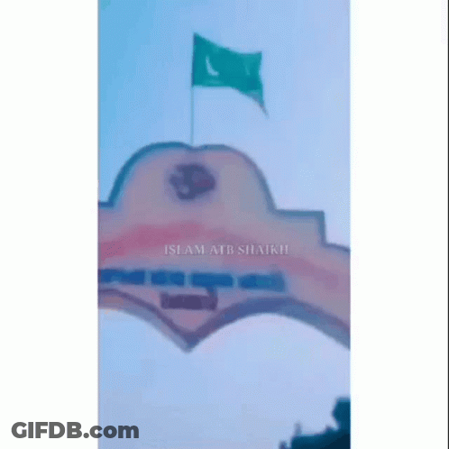 A Green Flag Is Flying In The Wind Over A Building GIF