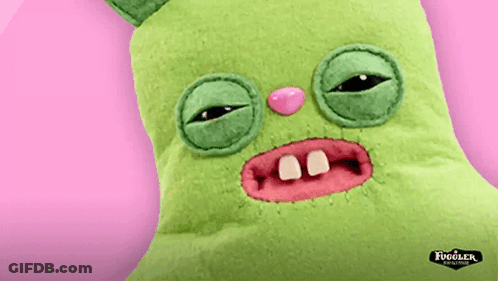 A Green Fugler Stuffed Animal With A Pink Nose And Teeth On A Pink Background GIF