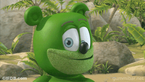 A Green Gummy Bear With Blue Eyes Is Smiling In A Jungle GIF