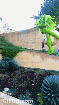 A Green Inflatable Elephant Is Sitting On A Concrete Wall GIF