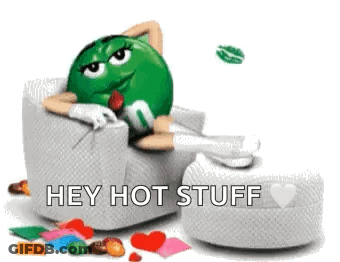 A Green M & M Is Laying In A Chair With Hearts Around Him And Says Hey Hot Stuff . GIF