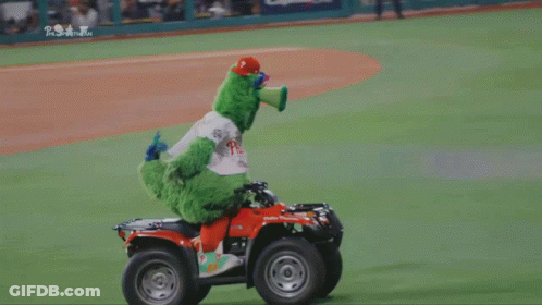 A Green Mascot Is Riding A Four Wheeler On A Baseball Field Sponsored By Phillies GIF