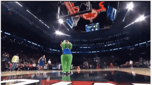 A Green Mascot Stands On A Basketball Court In Front Of A Scoreboard That Says Coca Cola GIF