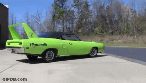 A Green Plymouth Superbird Is Parked On The Side Of The Road . GIF